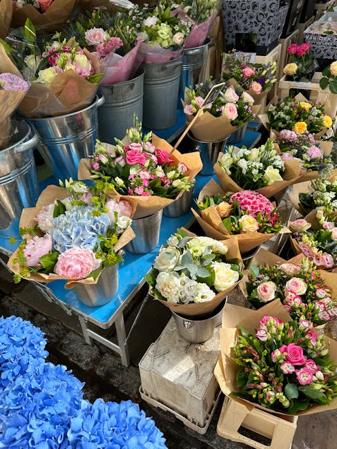 A vibrant display of freshly arranged flower bouquets and potted floral arrangements showcasing a variety of pastel-colored roses, hydrangeas, and other seasonal blooms wrapped in brown kraft paper an